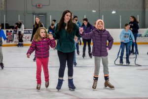 A mom and her two daughters are ice skating while holding hands
